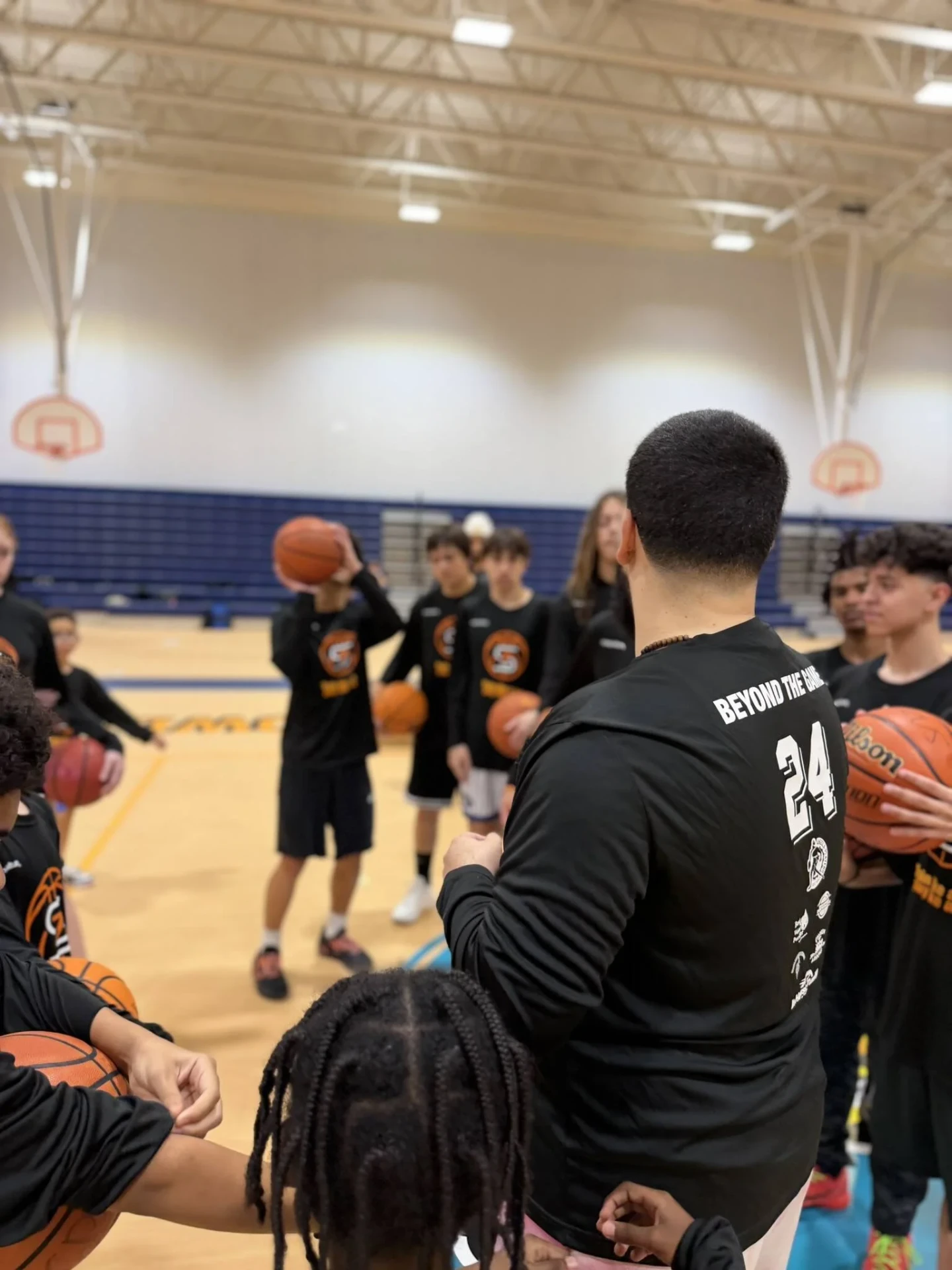 Coach addressing a group of players holding basketballs in the gym